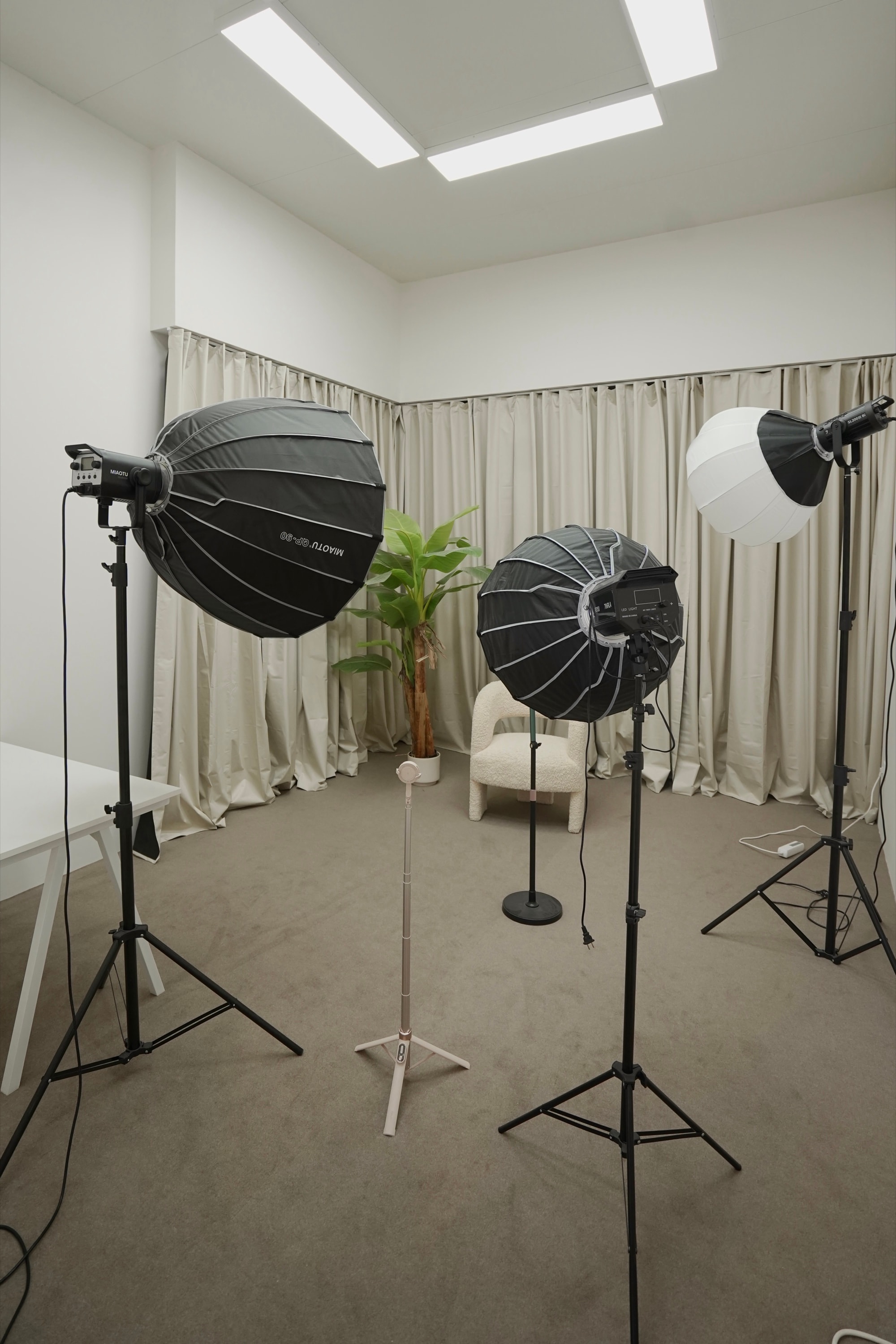 Beige live-streaming room — softboxes and a bouclé chair before a curtained backdrop