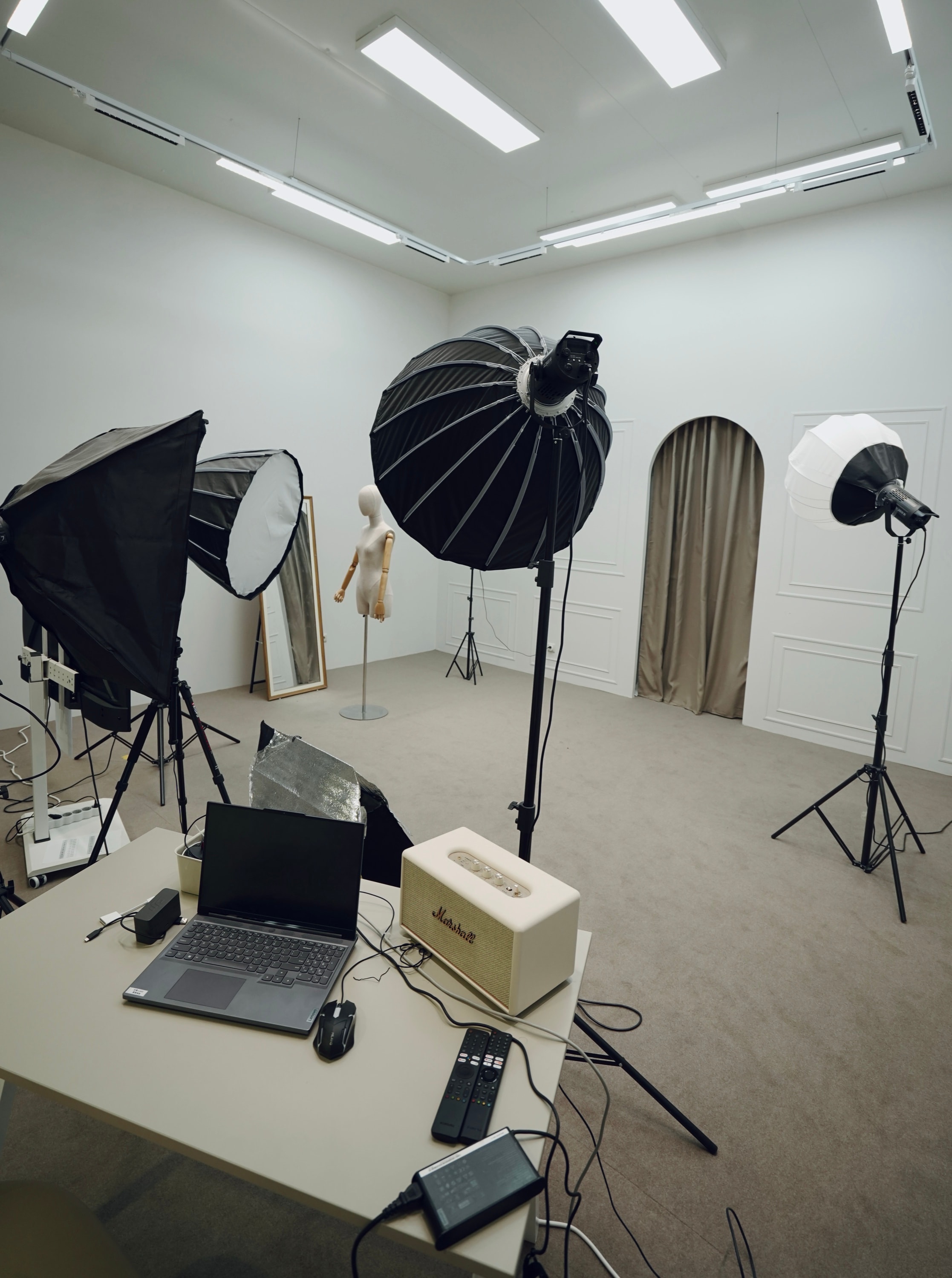 White production studio — softboxes, a mannequin form and an editing desk with a broadcast monitor